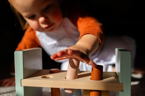 Toddler child playing with hammer pounding bench toy using hands to press blocks - Australian Stock Image