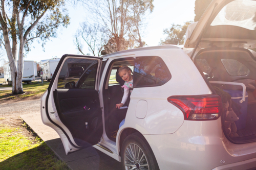 toddler girl climbing into car seat ready for holiday trip adventure - Australian Stock Image