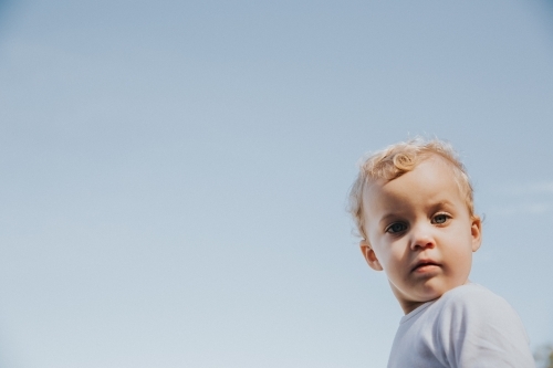 Toddler girl looking straight at the camera framed by blue sky - Australian Stock Image