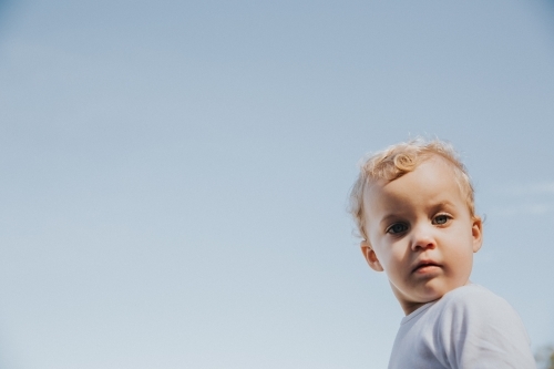 Toddler girl looking straight at the camera framed by blue sky