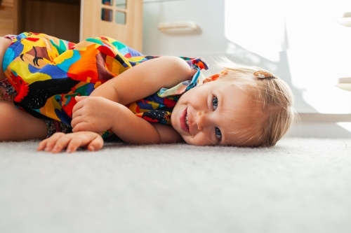 Toddler girl lying on floor of bedroom with morning light coming in the window - Australian Stock Image