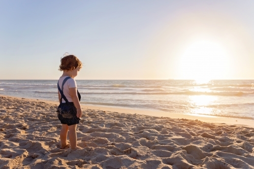 Toddler Girl On The Beach Looking Out To The Ocean At Sunset - Australian Stock Image