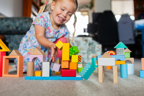 Toddler girl playing with colourful blocks on floor of home - Australian Stock Image
