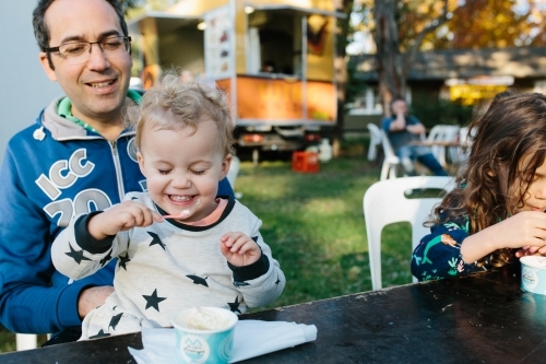Toddler girl smiling cheekily eating ice cream - Australian Stock Image