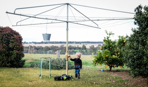 Toddler standing at hills hoist in country setting - Australian Stock Image