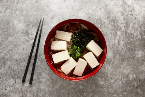 Tofu and noodle soup in red bowl - Australian Stock Image