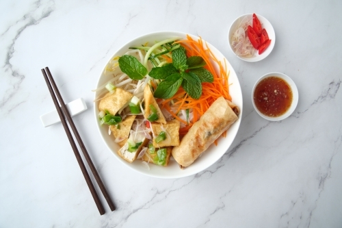 Tofu noodle salad topped with fried lumpia with salad dressing and chopsticks on the side. - Australian Stock Image