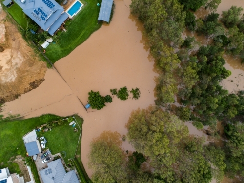 Top down aerial shot of dirty brown floodwaters rising up towards homes