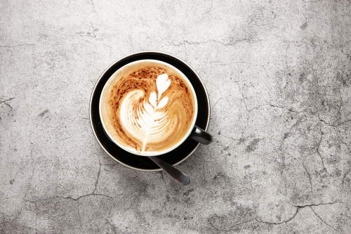 Top-down shot of cappuccino on black saucer - Australian Stock Image