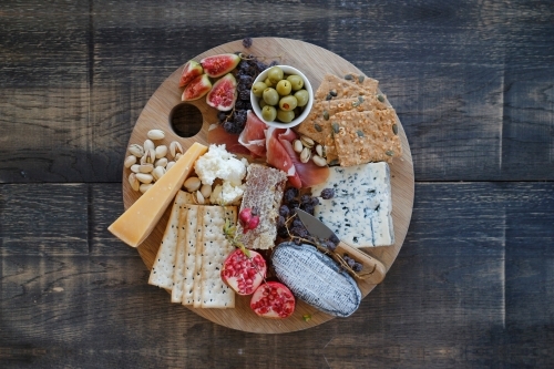 Top down view of cheese board on wooden table with cheese, crackers, olives and fruit