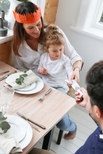 Top down view of family sharing a bon bon at Christmas table - Australian Stock Image