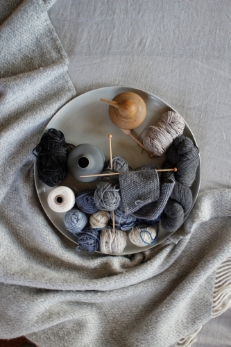 Top down view of knitting, wool and vases on grey blanket and linen