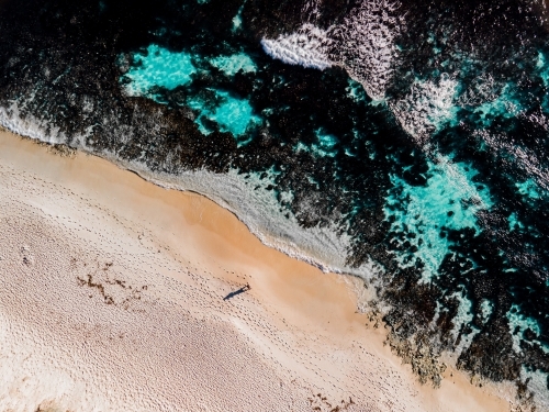 Top down view of lone person walking along sand next to reef on North Beach, WA