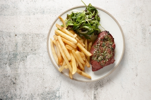Top down view of steak with salsa verde, chips and green salad - Australian Stock Image