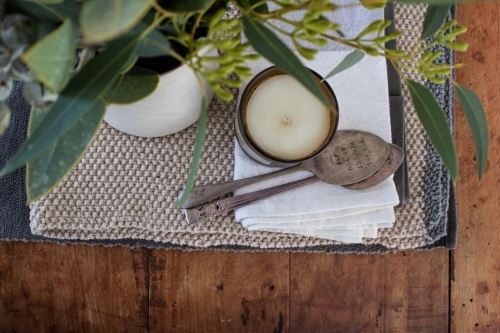 Top down view of table arrangement with flowers, knitted table runner, candle and antique spoons - Australian Stock Image