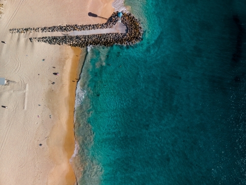 top shot of a beach front with a small walkway made of rocks, lamp post and white sand shoreline - Australian Stock Image