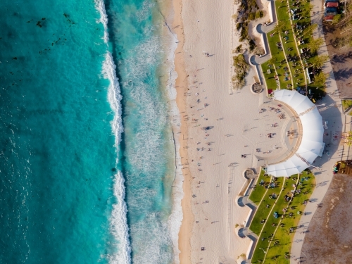 top shot of a beach with waves, white sand, people swimming, grass, trees and buildings - Australian Stock Image