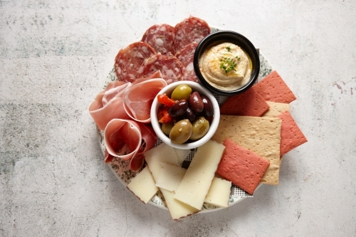 top shot of an antipasto platter on a white table with olives, cheese, cold cuts, and hummus - Australian Stock Image