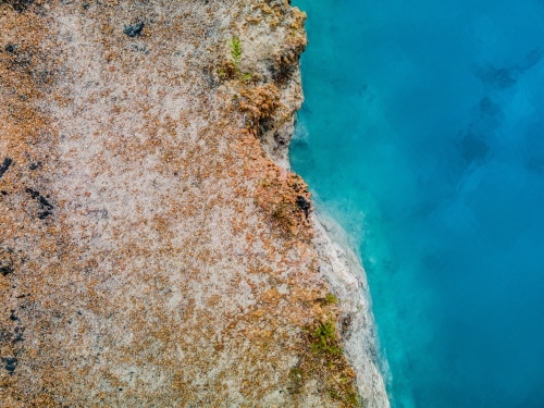 top view shot of a blue water meeting with a brown and white rock formation - Australian Stock Image