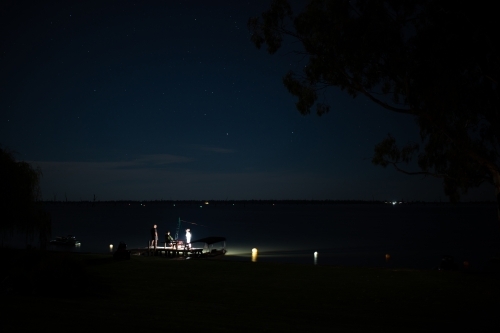 Torch lit people fishing on lake jetty at night - Australian Stock Image