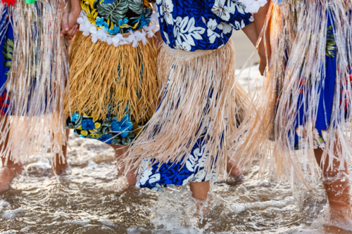 Torres Strait Islander children in traditional floral dresses and skirts standing together in ocean - Australian Stock Image