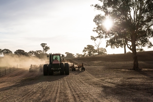 Tractor cultivating the field on a sunny day plough making dust - Australian Stock Image