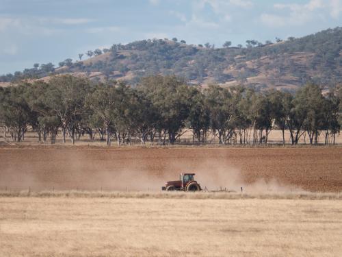 Tractor ploughing a paddock with dust swirling - Australian Stock Image