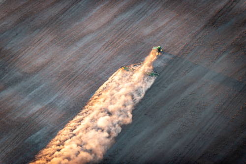 Tractor trailing dust across a dry paddock in early morning light, viewed from above - Australian Stock Image