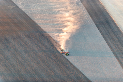 Tractor trailing dust across a dry paddock in early morning light, viewed from above - Australian Stock Image