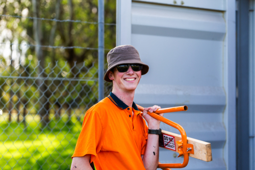 trade apprentice on worksite putting away equipment in shipping container storage at end of the day - Australian Stock Image
