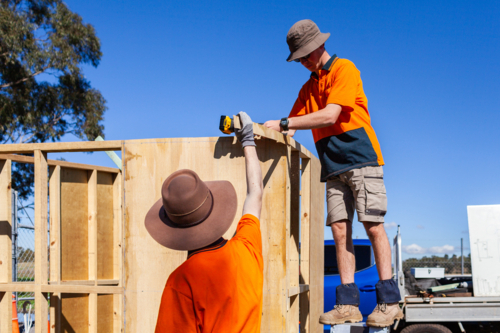 Trade apprentices learning hands on while constructing ticket booth in bright Australian sunlight - Australian Stock Image