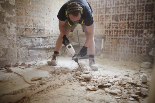 Tradesman jackhammering a floor in a home renovation - Australian Stock Image
