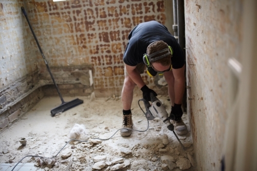 Tradesman jackhammering a floor in a renovation - Australian Stock Image