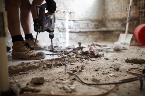 Tradesman jackhammering bathroom tiles in a home renovation - Australian Stock Image