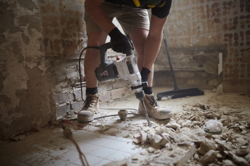 Tradesman jackhammering tiles in a bathroom - Australian Stock Image