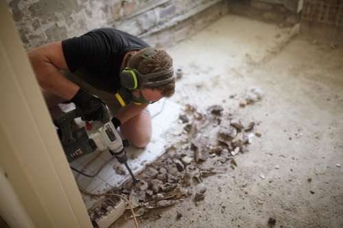 Tradesman jackhammering tiles on a bathroom floor in a home renovation - Australian Stock Image