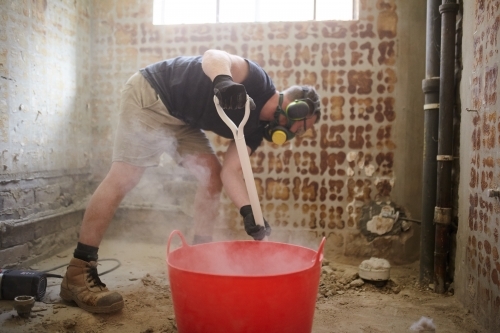 Tradesman shovelling debris into a bucket in a construction zone - Australian Stock Image