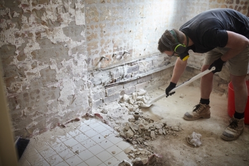 Tradesman shovelling debris off a floor in a construction site - Australian Stock Image