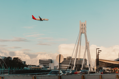 Traffic on road at Sydney Domestic Airport with plane flying overhead - Australian Stock Image
