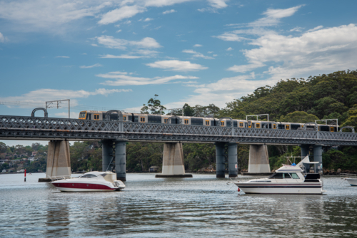 Train going over the rail bridge at Como in Sydney with moored boats in the foreground. - Australian Stock Image