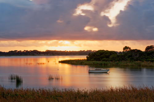 Tranquil Sunset over a Calm Coastal Inlet with a Solitary Boat - Australian Stock Image