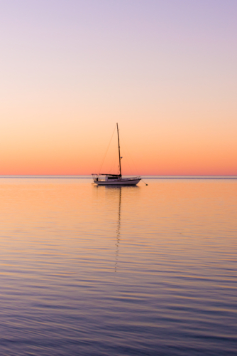 Tranquil yacht anchored at sea during a colourful sunset. - Australian Stock Image