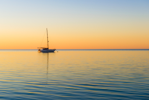 Tranquil yacht anchored at sea during a colourful sunset - Australian Stock Image