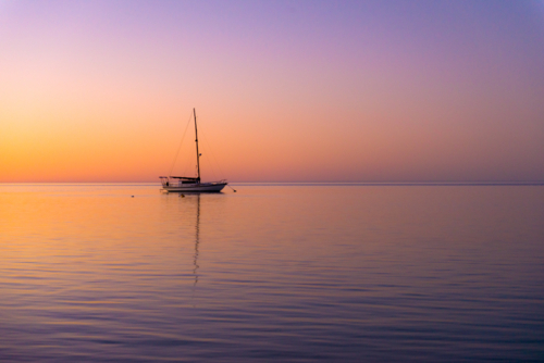 Tranquil yacht anchored at sea during a colourful sunset - Australian Stock Image