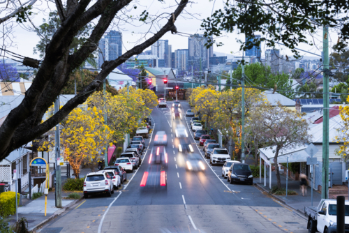 Tree lined urban street with golden foliage at dusk with light trails from passing vehicles - Australian Stock Image