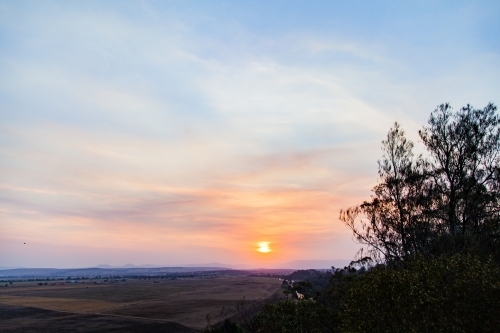 Trees silhouetted against smoke filled sunset sky - Australian Stock Image