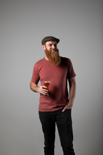 Trendy man with ginger beard and flat cap, holding a glass of beer
