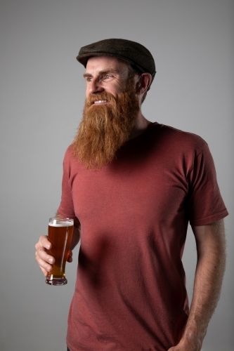Trendy man with ginger beard and flat cap, holding a glass of beer