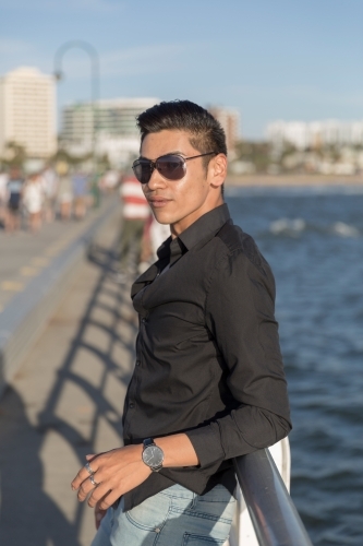 Trendy young man leaning against railing - Australian Stock Image