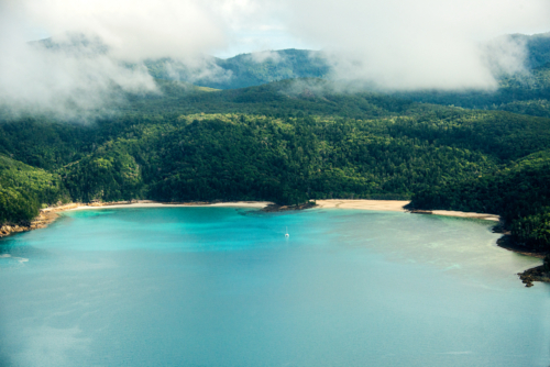 Tropical bay with turquoise water and beaches surrounded by lush rainforest and misty hills - Australian Stock Image